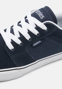 Námornícke modré skate topánky s bielymi šnúrkami, zvršok z semišu a textilu, herringbonový vzor po boku a značková nášivka blízko členka.