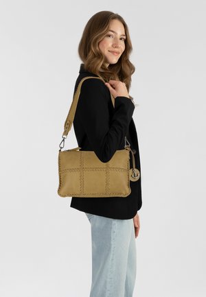 Sac à main en cuir tan avec un motif de grille cousu, forme rectangulaire, bandoulière réglable et un charme circulaire en argent. Porté avec un blazer noir.
