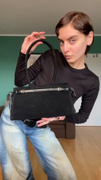 Τσάντα από μαύρο ύφασμα με δομημένο σχέδιο, δύο λαβές και λαμπερή ασημένια φερμουάρ. Λείο υλικό, μινιμαλιστικό σχήμα.