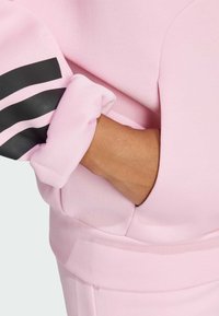 Ροζ φούτερ με μαύρες ρίγες στα μανίκια. Μαλακό ύφασμα με χαλαρή εφαρμογή και ανοιχτή τσέπη μπροστά.