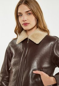 Giacca in pelle marrone con collo in shearling beige, chiusura con zip, tasche laterali e polsini a coste. Texture liscia e vestibilità sartoriale.