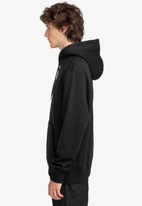 Felpa nera con cappuccio realizzata in mélange di cotone, caratterizzata da un cappuccio ampio, tasca frontale, polsini a coste e fit rilassato. Texture liscia, design minimale.