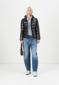 Svart dunjakke med kviltet design, kombinert med lyseblå stripete skjorte og løse blå jeans. Tilbehør: liten svart håndveske.