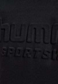 Zwarte sweatshirt met verhoogde zwarte letters waarop "HUMMR SPORTS" staat. De stof heeft een gladde textuur met een subtiele glans.