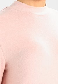Maglione rosa chiaro a collo alto realizzato in tessuto morbido. Texture liscia con un design aderente, che mette in risalto la zona del collo e del petto.
