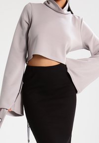 Kort, ljusgrå långärmad topp med hög krage och utsvängda ärmar, kombinerad med en figurnära svart kjol. Slät textur, minimal design.