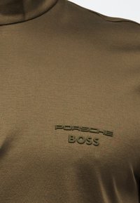 Ύφασμα ελιάς με ανάγλυφο λογότυπο «PORSCHE BOSS» στο ίδιο χρώμα στην περιοχή του στήθους σε ένα επάνω μέρος.