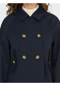 Abrigo azul marino de doble botonadura con grandes botones de latón, cuello con muesca y bolsillos laterales. Fabricado en una tela suave y duradera.