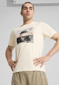 Cremfarvet bomulds t-shirt med et bjerggrafik, topografiske linjer og teksten "PUMA SEASONS" nederst. Korte ærmer.