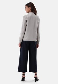 Blusa grigia chiara con colletto e maniche lunghe, abbinata a pantaloni larghi blu navy e tacchi neri con cinturini. Texture del tessuto liscia.