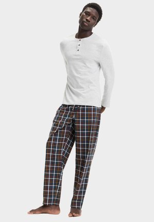 Camisa blanca de manga larga tipo henley con tres botones, combinada con pantalones a cuadros en azul, verde y marrón, con cinturilla elástica y bolsillos.