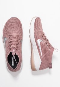 Pink knit training shoes with a textured upper, silver Nike swoosh, and a white speckled sole. Features a pull tab and lace closure.