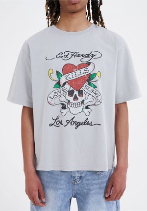T-shirt en coton gris clair avec un impression graphique colorée d'un crâne avec un cœur rouge et le texte "L'AMOUR TUE SLOWLY" en dessous de "Los Angeles."