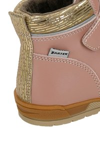 Růžová kožená bota s texturovaným zlatým detailem kolem límce, suchým zipem a odolnou gumovou podrážkou se vzorovaným profilováním.