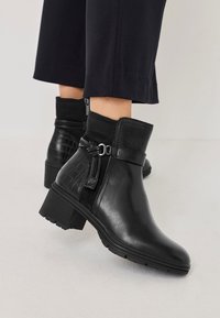 Bottines noires avec un dessus en cuir lisse et un accent en imprimé crocodile texturé, équipées d'une fermeture éclair sur le côté et d'un talon épais.