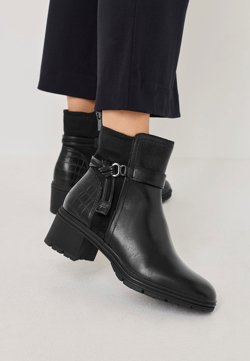 Bottines noires avec un dessus en cuir lisse et un accent en imprimé crocodile texturé, équipées d'une fermeture éclair sur le côté et d'un talon épais.
