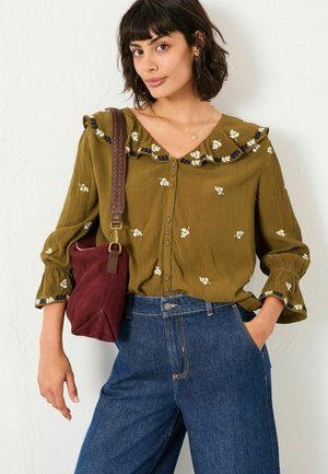 Olive green, button-up blouse with floral embroidery, ruffled collar, and bell sleeves. Paired with high-waisted blue denim jeans and burgundy bag.
