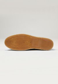 Semelle de chaussure en caoutchouc avec une surface texturée et à motif. La couleur est brun clair avec une finition lisse et des détails de taille en relief.
