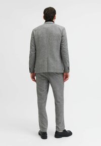 Completo grigio con giacca aderente e pantaloni abbinati, caratterizzato da un colletto nero e scarpe nere, visto da dietro.