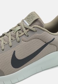 Svijetlosmeđi atletski tenisice s teksturiranim gornjim dijelom, crni Swoosh logo i fleksibilna bijela potplat. Ima bež vezice i oznaku.