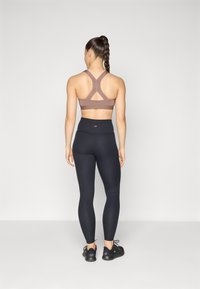 Soutien-gorge de sport marron avec un dos croisé, associé à un legging noir côtelé taille haute et des chaussures de sport noires, vu de dos.