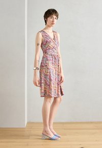 Robe colorée à motif zigzag avec une taille ceinturée, un design sans manches et une jupe évasée. Portée avec des sandales à talons bloc bleu clair.