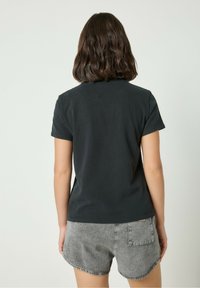 Must have lühikeste varrukatega must T-särk ümmarguse kaelusega, sile puuvillane tekstuur ja relaxed fit, koos hallide teksashortsidega.