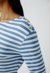 Blau-weiß gestreiftes Langarmshirt aus strukturiertem Stoff mit silbernen Knopfakzenten an der Schulter. Modernes, figurbetontes Design.