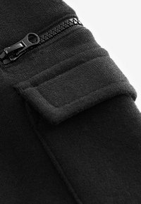 Sort fleece stof med en lynlås lomme, der har et glat greb, blød tekstur og pæne stikninger langs kanterne.