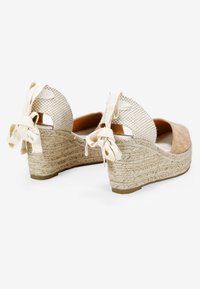 Sandalias de cuña con una zona de dedos de ante beige claro, parte trasera de tela trenzada y tacón de cuña con textura de cuerda y acentos de cinta.