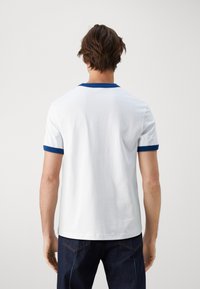 Camiseta blanca de manga corta con cuello y puños de canalé azul, hecha de tela de algodón, que presenta una textura suave y un diseño sencillo.