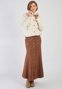 Kremowa kurtka z mieszanki wełny z przednimi guzikami i kieszeniami, zestawiona z brązową maxi spódnicą zamszową z złotymi guzikami i kieszeniami po bokach.