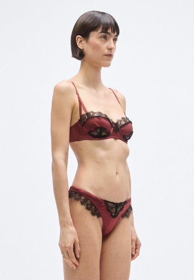 Bordó szatén fehérnemű szett fekete csipkével díszített melltartóval és bugyival, állítható pántokkal és hullámos szegélyekkel.