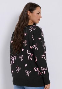 Mustapaita, jossa on vaaleanpunaiset nauhat ja sydänkuviot, rento malli ja ribbiohut hihansuut. Pehmeää neulottua kangasta, jossa klassinen pyöreä kaula-aukko.