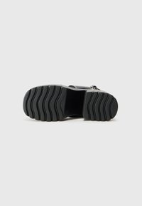 Black rubber footwear sole with textured grip pattern, featuring broad grooves for traction and support, designed for comfort and durability.