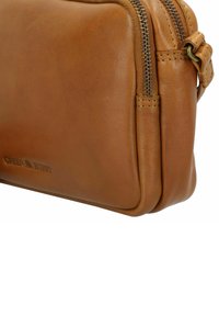 Borsa a tracolla in pelle marrone con una trama liscia, caratterizzata da una chiusura a zip e una forma arrotondata. Logo discreto impresso sul lato.