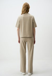Top in maglia a coste beige con maniche corte abbinato a pantaloni larghi coordinati, entrambi caratterizzati da una vestibilità comoda e una texture soffice.