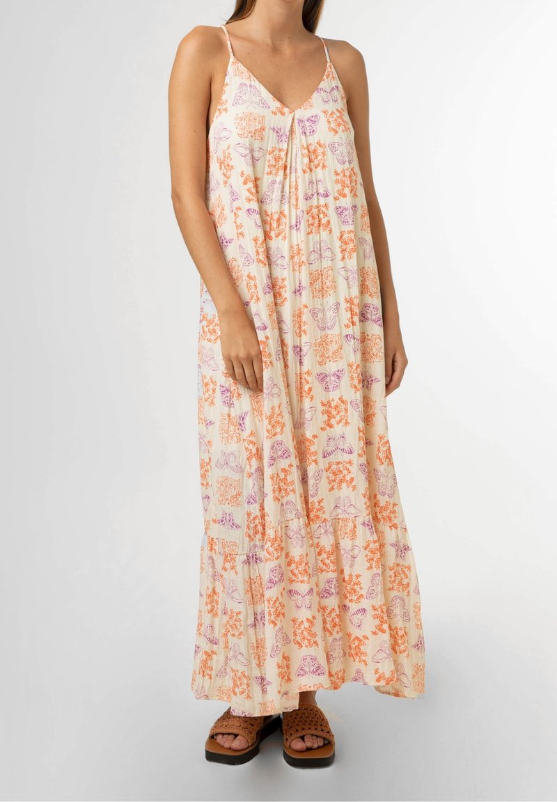 Femme portant une robe maxi fluide sans manches avec des imprimés de papillons orange et violet ainsi que des fleurs, associée à des sandales marron à enfiler.