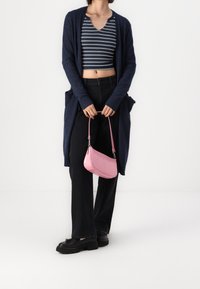 Cárdigan azul marino, top recortado de rayas, pantalones de pierna ancha negros, zapatos de plataforma negros y un pequeño bolso texturizado rosa con correa de hombro.