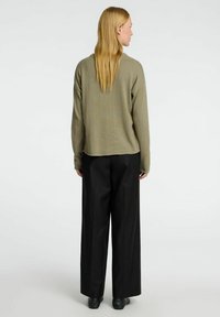 Olivgrüner Strickpullover mit langen Ärmeln, kombiniert mit schwarzen weit geschnittenen Hosen. Sanfte Textur und lockerer Schnitt, mit abgerundetem Saum.