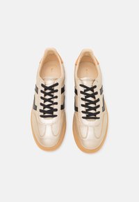 Metallic gold sneakers with black stripes, round toe, black laces, and gum outsole. Smooth leather texture, minimalist design.