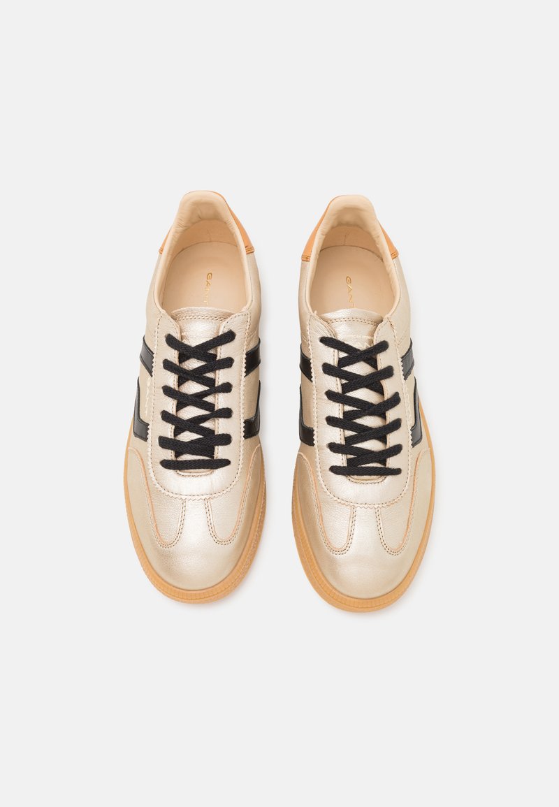 Metallisch goldene Sneakers mit schwarzen Streifen, runder Zehenform, schwarzen Schnürsenkeln und Gummisohle. Glatte Ledertextur, minimalistisches Design.