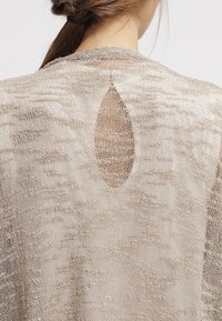 Beige open-knit cardigan with a textured finish, featuring a rounded neckline and a pear-shaped cutout detail at the back.