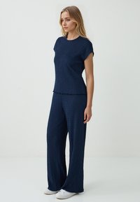 Marineblauwe textuur tweedelige outfit met een korte mouw top en wijde broek, aangevuld met witte sneakers.