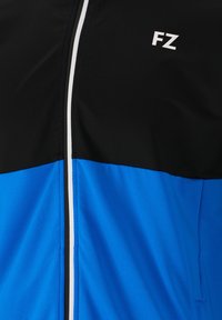 Svart och blå sportjacka med vit dragkedja, med en färgblockdesign och bokstäverna 'FZ' i vitt på den övre delen.