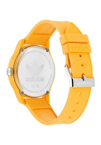 Montre en silicone jaune avec un boîtier rond, dos en acier inoxydable, bracelet texturé et boucle en argent. Affiche le logo Adidas sur le bracelet.