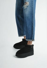 Stivaletti neri in suede con una spessa suola platform, caratterizzati da una punta arrotondata e un design con risvolto. Indossati con jeans in denim blu strappati.