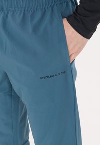 Ljusblå sportbyxor i glattyg. Har elastisk midja och sidofickor. Märket "ENDURANCE" är tryckt i svart.