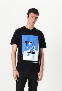 Camiseta de algodón negra con un estampado gráfico en azul y blanco de una cara con gafas de sol. Corte recto, mangas cortas, cuello redondo.