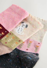 Mehrfarbige Socken mit Mustern: pink mit Sprenkeln, eine cremefarbene Socke mit einem Hundedesign und eine dunkle Socke mit bunten Sprenkeln und floralen Akzenten.